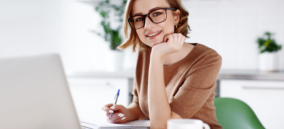 Mujer trabajando sonriendo mientras apunta en un libreta