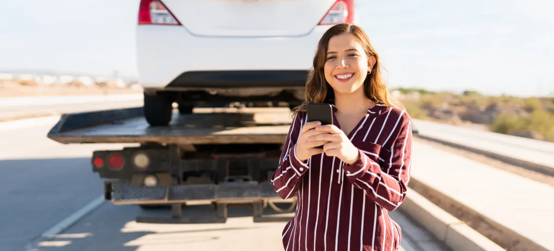 Mujer sonriente con un móvil en sus manos y una grúa con un coche de fondo