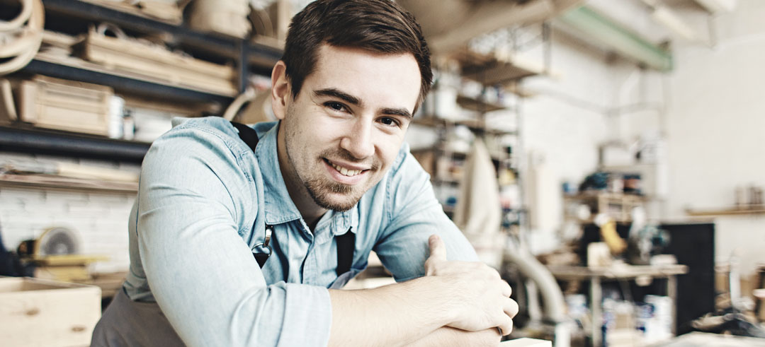 Chico joven sonriendo con los brazos sobre la mesa en su fábrica